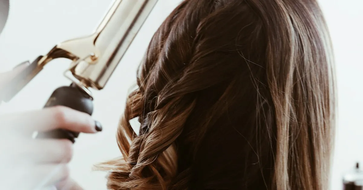 Coiffeuse bouclant au fer une chevelure aux reflets de balayage