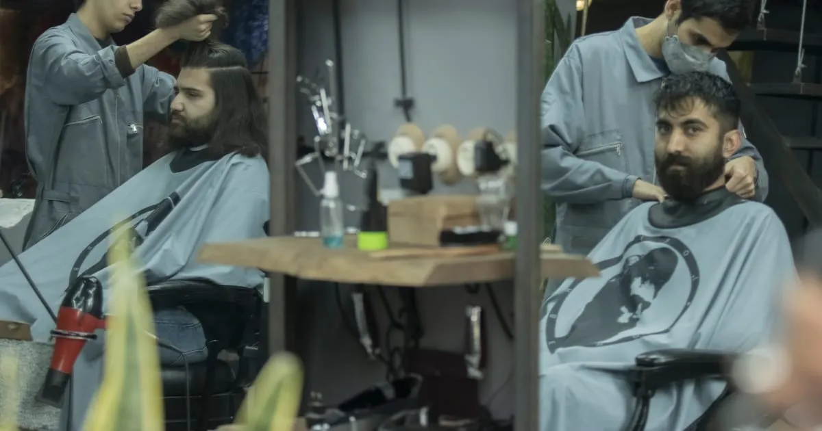 Deux barbiers coupant les cheveux de clients installés dans leurs fauteuils, dans un barbershop