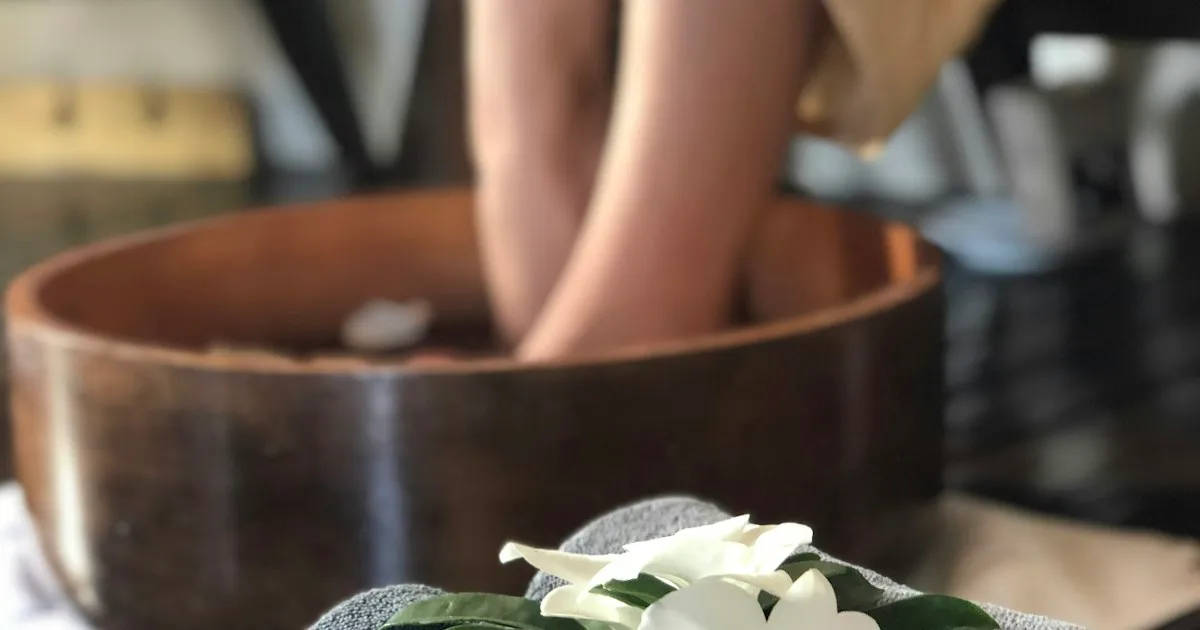Pieds plongés dans un bain tiède au creux d'une vasque en bois, avant un soin de beauté des pieds en institut