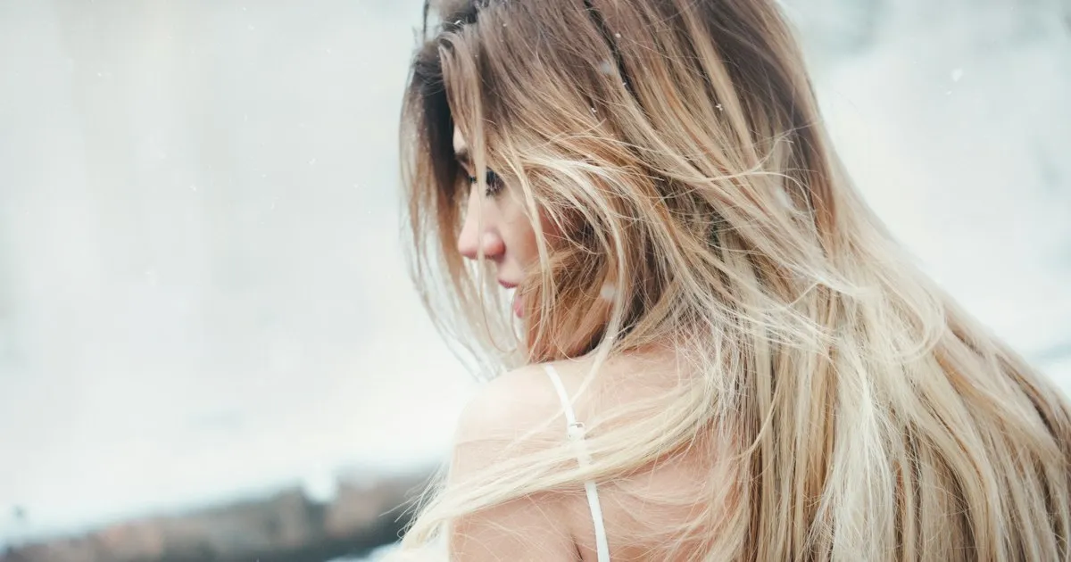 Femme vue de dos aux longs cheveux blond clair décolorés, légèrement ébouriffés par le vent