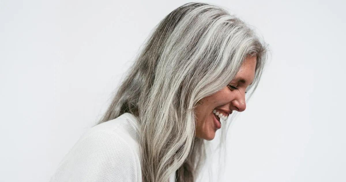 Femme souriante aux longs cheveux gris argentés, vue de profil sur fond blanc