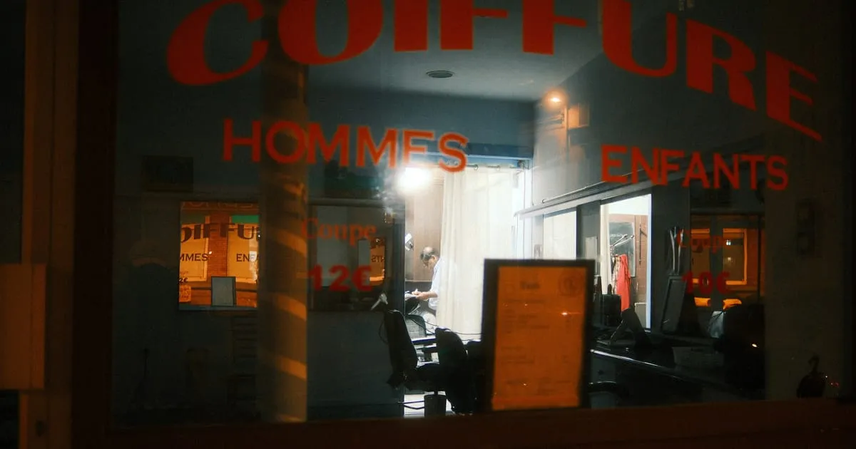 Vitrine éclairée d'un salon de coiffure hommes et enfants, ouvert à la tombée de la nuit
