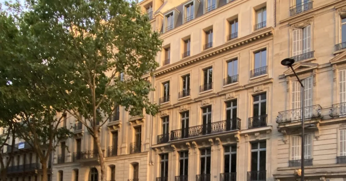 Façade d'un immeuble haussmannien en pierre de taille avec balcons en fer forgé, bordée d'arbres, à Paris