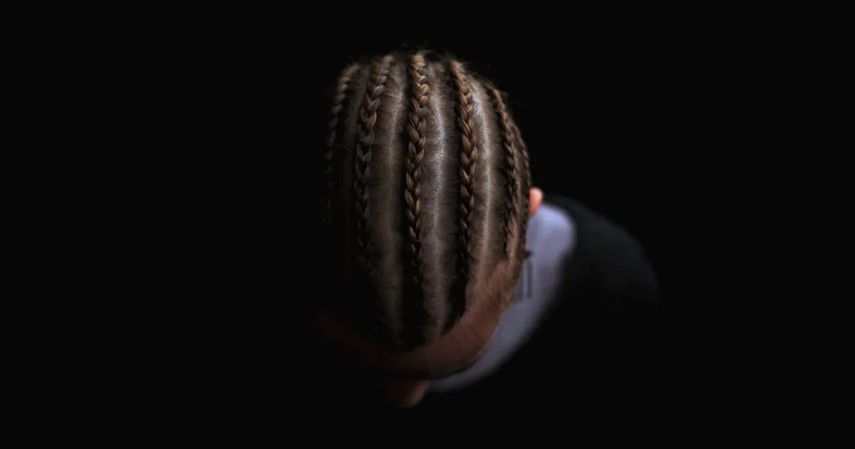 Tête vue de dessus coiffée de nattes collées régulières sur des cheveux crépus, sur fond noir