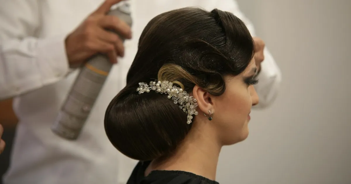 Coiffeur finalisant le chignon bas d'une mariée orné d'un bijou de cheveux en perles