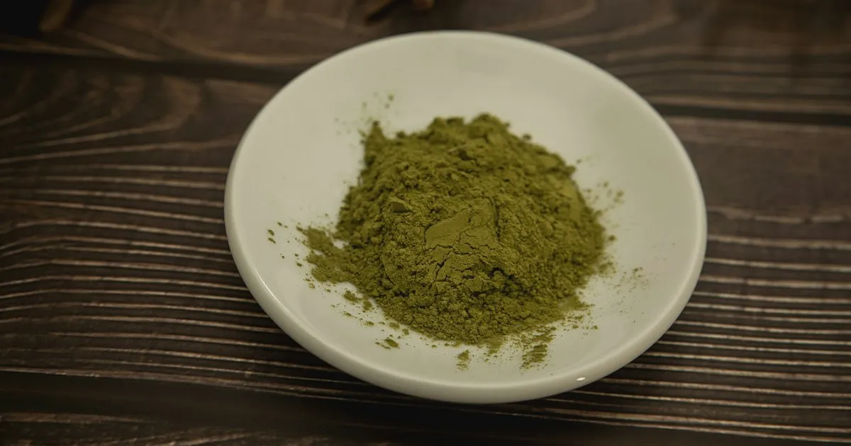 Poudre de henné verte dans une coupelle blanche posée sur une table en bois, prête à être préparée pour une coloration végétale