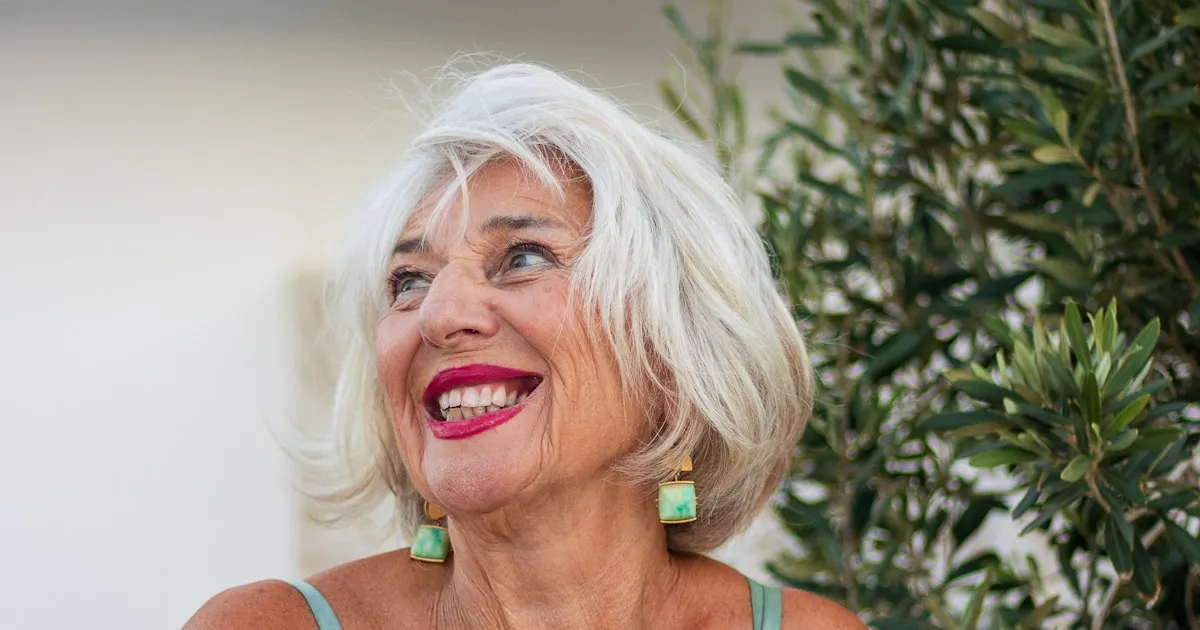 Femme d'une soixantaine d'années souriante, coiffée d'un carré blanc argenté en mouvement