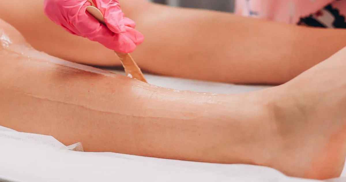 Esthéticienne appliquant de la cire à épiler sur une jambe avec une spatule