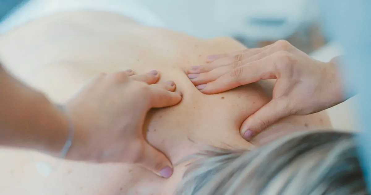Mains d'une praticienne massant le dos d'une cliente allongée en institut