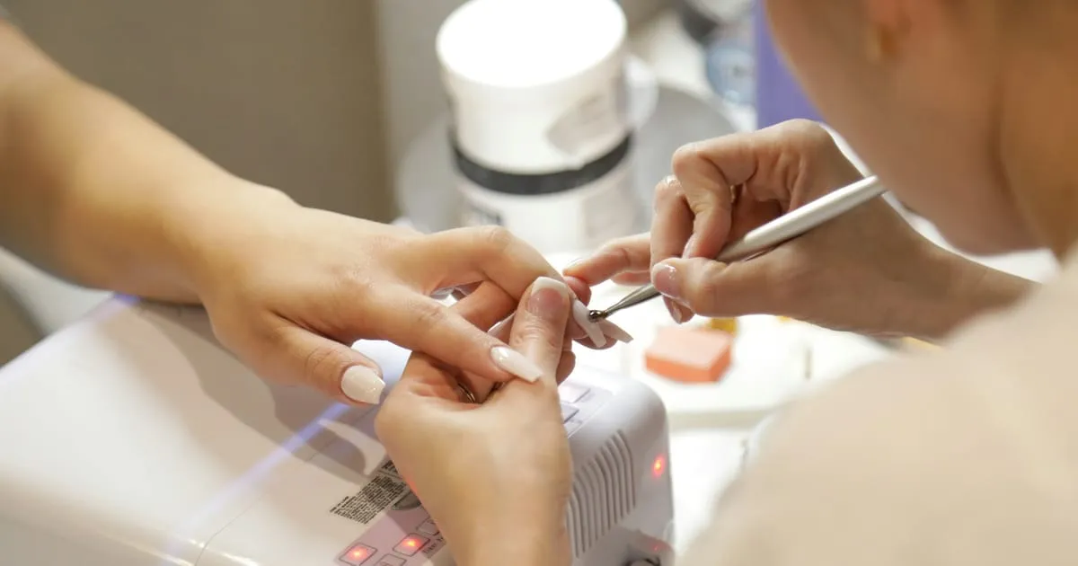 Prothésiste ongulaire repoussant les cuticules d'une cliente avant une pose, sur une table de manucure