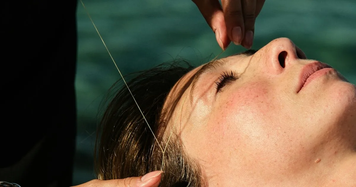 Femme allongée les yeux fermés pendant une épilation des sourcils au fil